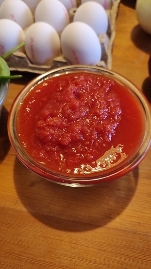 tomato puree in a glass bowl and eggs in the background