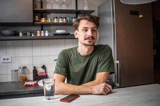 One young man, young man, with mustache and beard, hipster culture and lifestyle, sitting in the kitchen at the bar, portrait of a young man in his apartment where he just moved