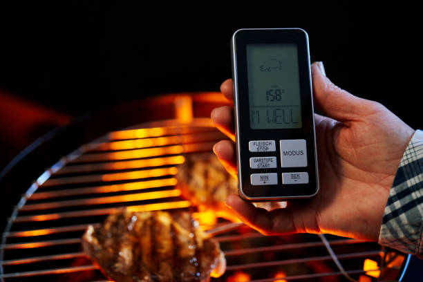 Digital cooking counter with barbecue grill in background. Counting cooking time in nature on a family picnic using a digital BBQ counter.