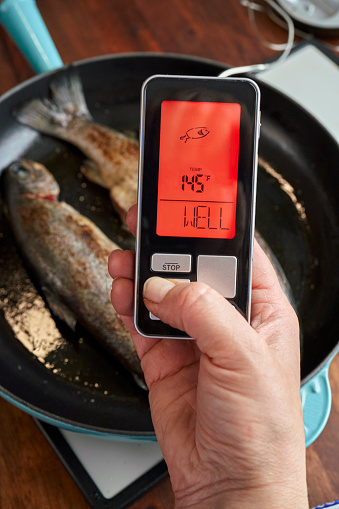 Food Safety - Checking the Right Temperature with Digital Thermometer on Roasted Trout Fish in a Pan