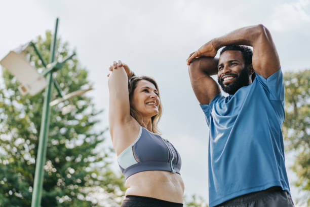 pareja de amigos estirándose para hacer ejercicios físicos - warming up fotos fotografías e imágenes de stock