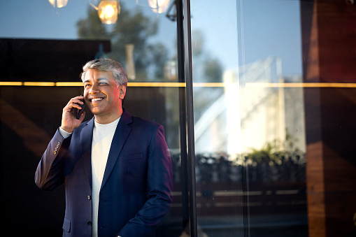 Cheerful businessman using mobile phone at office seen through glass window