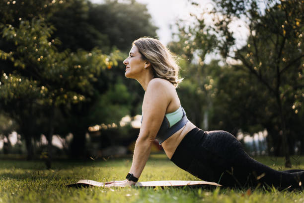Woman practicing physical exercise on mat in public park stock photo