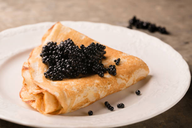 deliciosa panqueca fina com caviar preto em um prato, close-up - appetizer caviar gourmet blini - fotografias e filmes do acervo