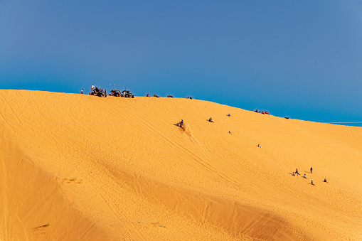 Unrecognizable far people sitting in the gold colored dune with buggy cars parked in the summit. Sahara desert of Taghit, Algeria. Sunny day with a blue sky