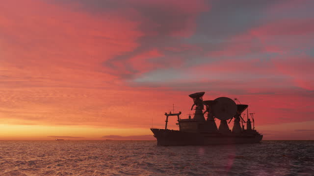 Scientific ship with satellite dishes in silhouette in the sea in a romantic sunset illumination