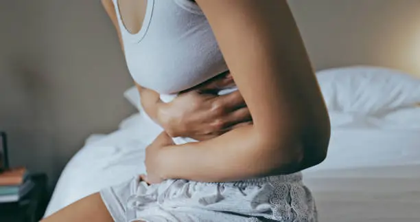 Photo of Menstruation, stomach ache and hands of woman in bedroom for indigestion, cramps and illness. Frustrated, gas and stress with girl on bed for constipation, bloating and intestine problems at home