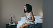 istock Menstruation, sick and stomach ache with black woman in bedroom for indigestion, cramps and illness. Frustrated, gas and stress with girl on bed for constipation, bloating and intestine problems 1462664404
