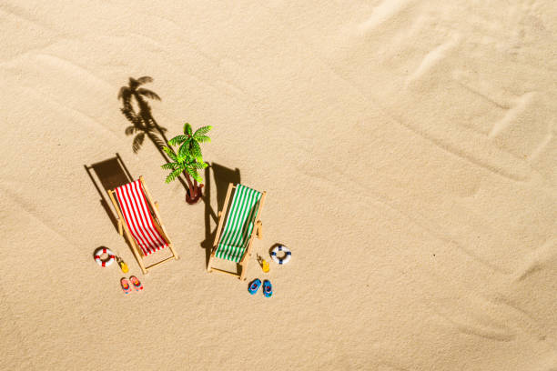 vue aérienne de deux chaises longues, transat, salon, verre de jus d’orange, tongs, lifebuoy, palmier sur plage de sable fin. concept d’été et de voyage. minimalisme - beach tropical climate palm tree deck chair photos et images de collection
