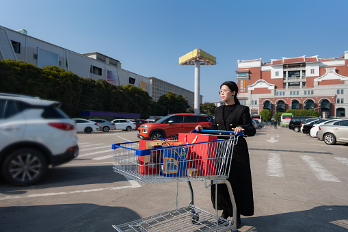Asian lady pushing trolley towards her car after shopping