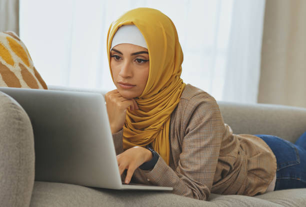 istock Muslim woman reading email, relaxing on sofa and elearning from laptop at home. Young arab student typing academic blog, remote work for freelance job or studying in the living room with wifi 1462668227