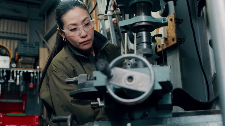 Medium shot of a mid adult female using machining equipment at a metal fabrication workshop