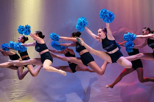 athletes perform on stage, young cheerleaders perform at the cheerleading championship, girls in a jump, girls are holding pompons, hands raised up, side hurdler