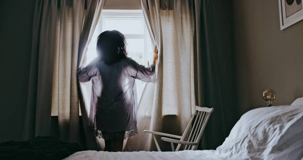 camera da letto, finestra e donna che aprono le tende pronte per la mattina e guardando l'alba. vista posteriore, sveglia e signora che si rilassa nella sua casa o casa dopo aver dormito, riposare e godersi la luce del sole - curtain window women opening foto e immagini stock