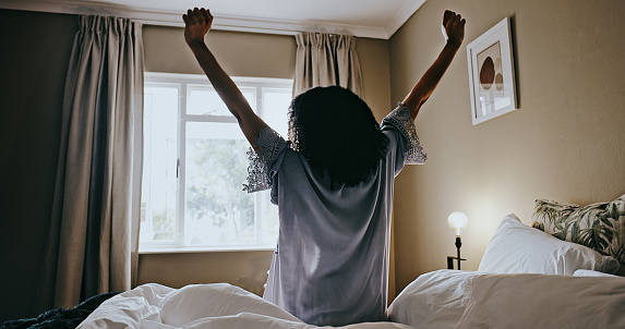 Back, woman and waking up with sunrise, stretching and morning in bedroom, sleepy and rest. Female, lady and young person on bed, relax and prepare to start the day, mindset and early stretch at home