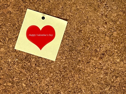 Happy Valentine's Day word on yellow sticky pad pinned on cork board