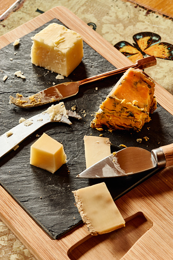 Three different cheeses on a cheese board with cheese knives. Clockwise from the top, English Cheddar, Harrogate Blue and Tomme de Savoie.