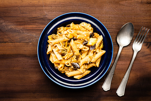 High angle view of Italian pasta penne in blue dish ready to eat with cheese over rustic pine wood table.