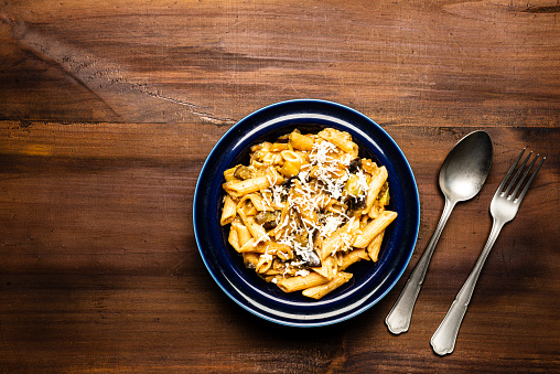 High angle view of Italian pasta penne in blue dish ready to eat with cheese over rustic pine wood table.