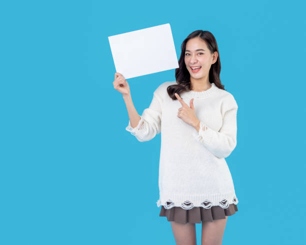 istock Your text here. Young excited woman holding empty blank board. Colorful studio portrait with light blue background. Woman holding blank empty banner pointing finger to one self smiling happy and proud 1462678151