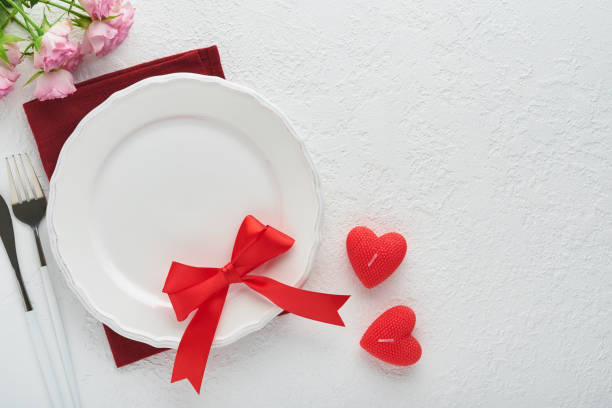 istock Valentines day romantic table setting. Empty or closeup of a dinner black plate, knife, fork and decorative silk hearts on white background. Holiday concept. Copy space for inscriptions. 1462678380