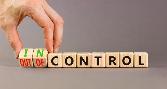 In or out of control symbol. Concept words In control and Out of control on wooden cubes. Businessman hand. Beautiful grey table grey background. Business in or out of control concept. Copy space.