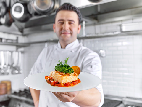 Chef serving a gourmet salmon dish in a commercial kitchen