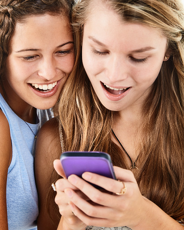 Cheerfully scandalized young woman and teenager holding their colorful smart phones, gasping at what they see on them.