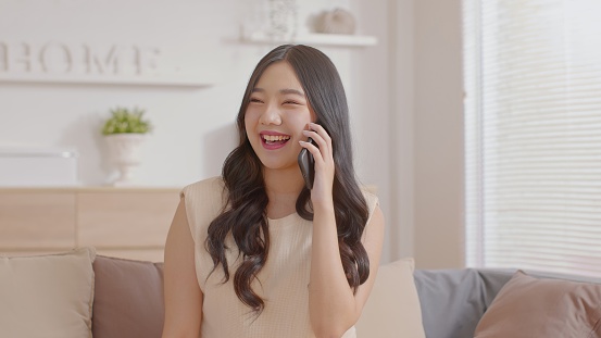 Asian young woman answer the phone and talking with positive and happiness emotional.Attractive female talkin in smartphone smile and cheeful with good news and good moment at home