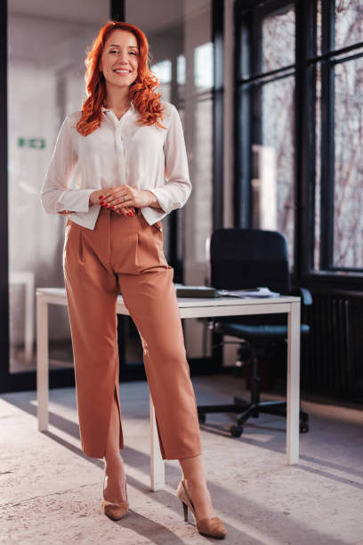 Full length portrait of confident young businesswoman standing in office looking at camera while smiling. stock photo