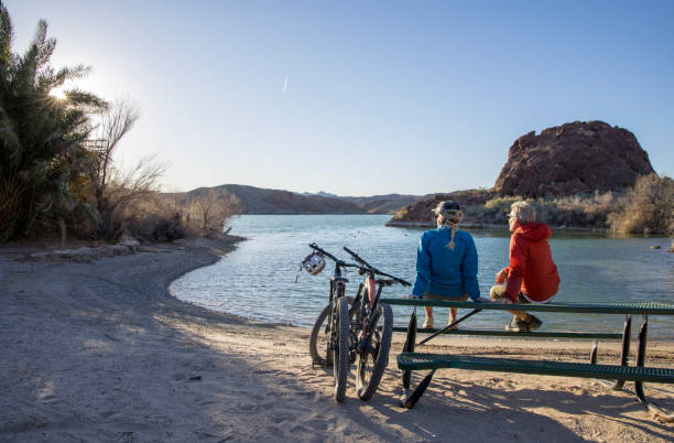 un couple de cyclistes de montagne matures se détend au bord du lac - senior couple cycling beach bicycle photos et images de collection