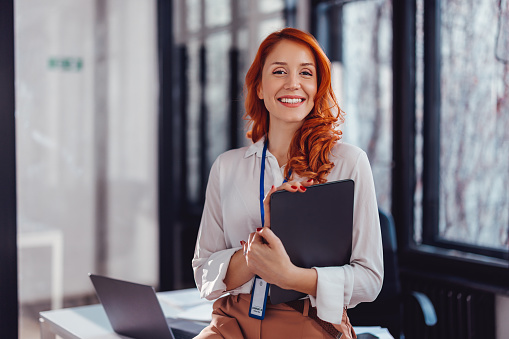 Attractive business woman in formal wear is holding a digital tablet and looking at the camera with a smile.