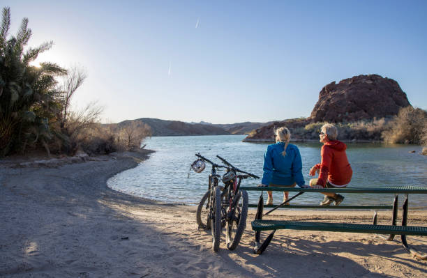 un couple de cyclistes de montagne matures se détend au bord du lac - senior couple cycling beach bicycle photos et images de collection