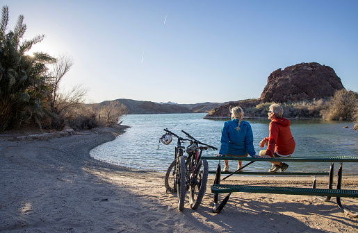 Mature mountain biking couple relax by empty lakeshore