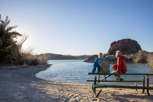 casal maduro de caminhadas relaxa à beira do lago vazio - sunrise beach couple hiking - fotografias e filmes do acervo