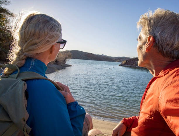 casal maduro de caminhadas relaxa à beira do lago vazio - sunrise beach couple hiking - fotografias e filmes do acervo