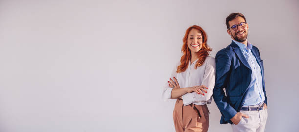 Business partners posing in front of gray background, looking at camera and smiling. stock photo
