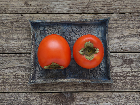 Persimmon fruits on a blue ceramic tray on a wooden background, table top view. Close up photo of kaki fruit with details. Photo directly from above.