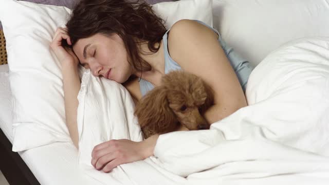 Young woman sleeping on her side in bed hugging her dog