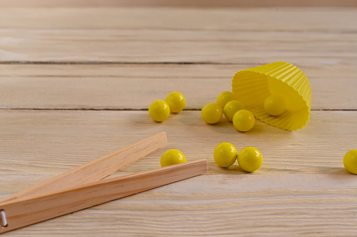 yellow balls and wooden tweezers for the development of fine motor skills for children. on a wooden background.