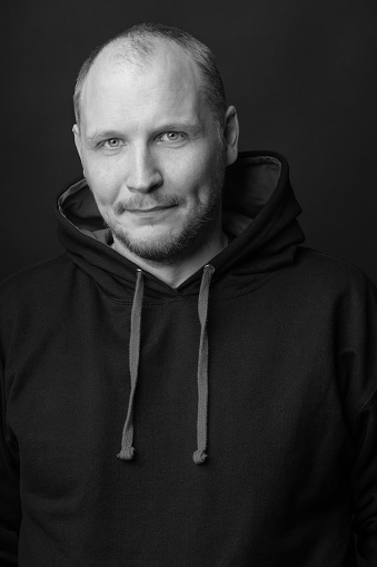 Lifestyle and fashion concept. Close-up man studio portrait. Model wearing black hoodie sweatshirt with laces and copy space. Black studio background. Man looking at camera. Black and white image