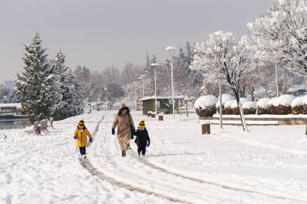 mother and son walking together in public park under snow. they wore a winter coat and scarf. walking in wooded area covered with snow. Shot with a full-frame camera in daylight.