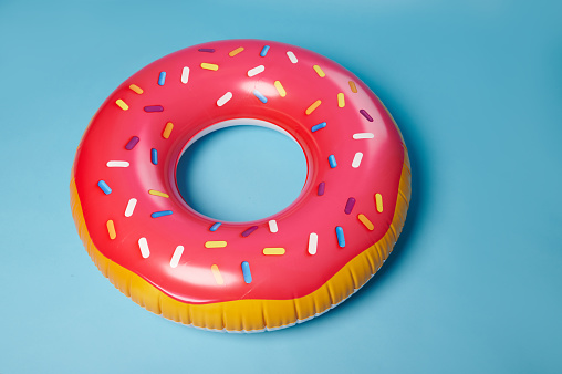 Bright colorful pink inflatable swim ring donut, a lifebuoy, isolated on blue color background. Accessory for safety swimming in swimming pool or sea. Summer holidays and entertainment concept.