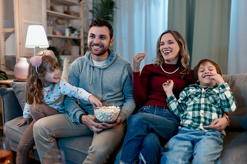 Young happy family enjoying on the sofa while watching something funny on the TV.