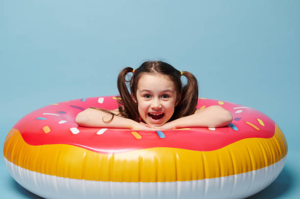 menina bonita em maiô, poses dentro de um anel de banho, fundo azul. conceito de entretenimento de verão, férias e praia - swimming tube inflatable circle - fotografias e filmes do acervo