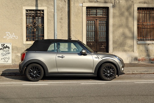 Udine, Italy. February 4, 2023. Gray convertible Mini Cooper in a city street with abandoned old house on background