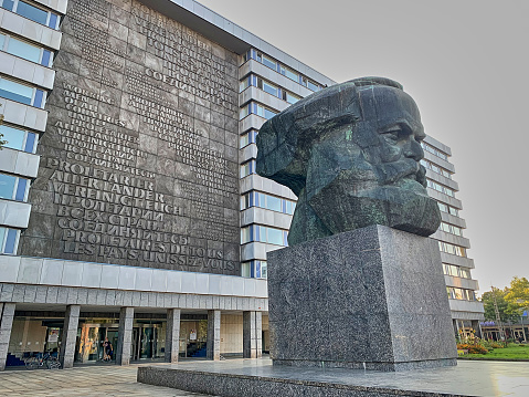 Chemnitz, Germany - 09 08 2021: Monument of Karl Marx infront of a building displaying the text of his communistic thesis in large letters carved in stone.