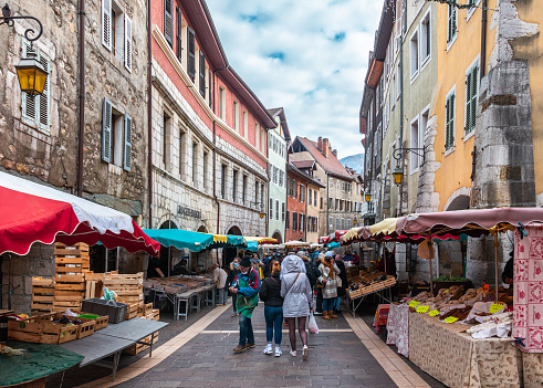 Annecy, France - January 7, 2022: People buying vegetables and fruits on the market in medieval historical old town of french Annecy with colorful facades