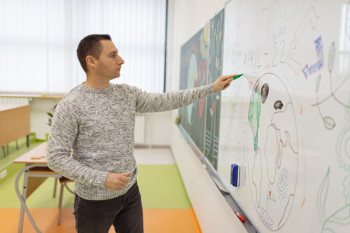 A side view of one young male professor giving a lecture about ecology and saving the planet Earth and drawing on a board.