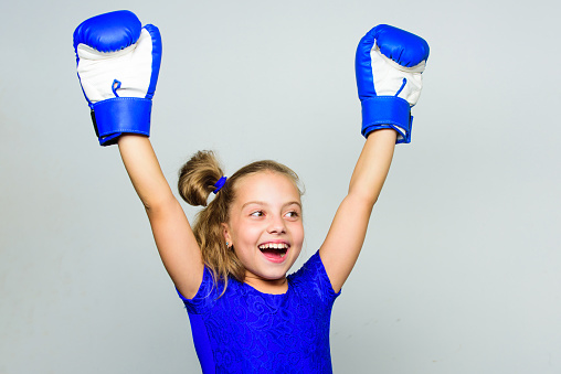 Girl child happy winner with boxing gloves posing on grey background. Feminist movement. She feels as winner. Upbringing for leadership and winner. Strong child proud winner boxing competition.